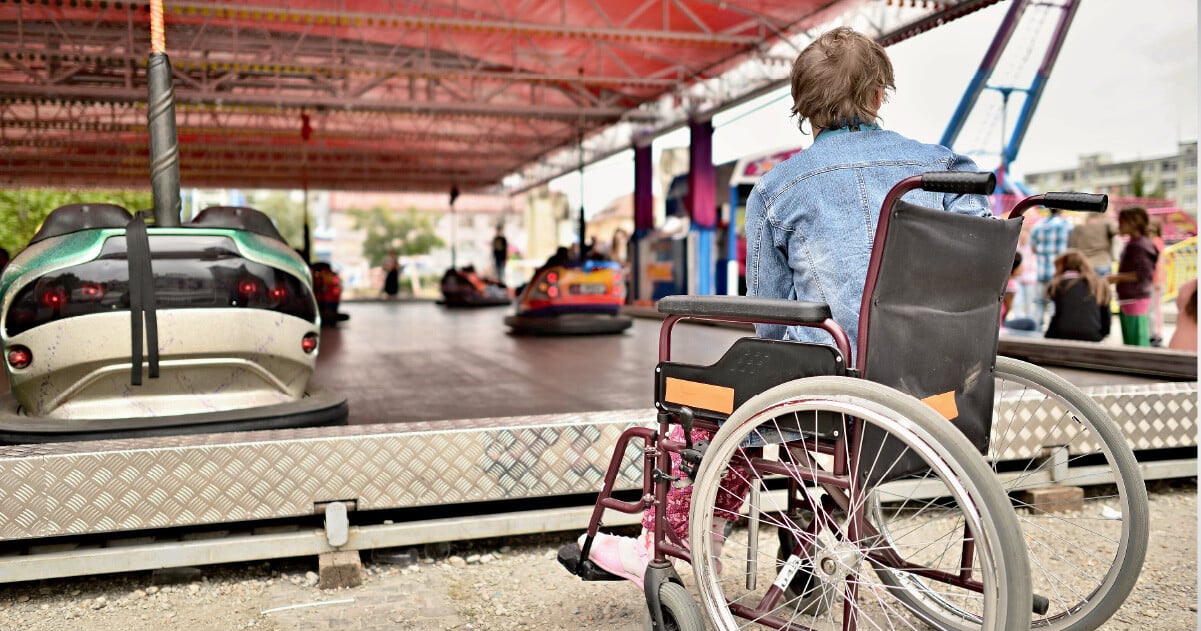 woman in wheelchair watches a bumper car game from the sidelines